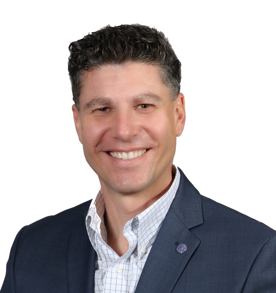 Man with dark hair, smiling, wearing a suit and with a lapel pin